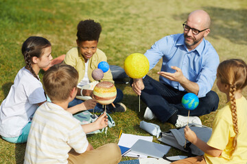 Wall Mural - High angle portrait of male teacher pointing at planet model and smiling while enjoying outdoor astronomy class with group of children, copy space