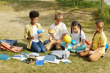 full length portrait of multi-ethnic group o children sitting on green grass and holding model plane