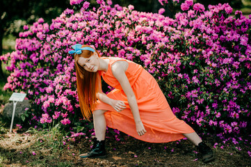 Strange young girl with long red hair, pretty face in a summer orange dress have a good time in the garden