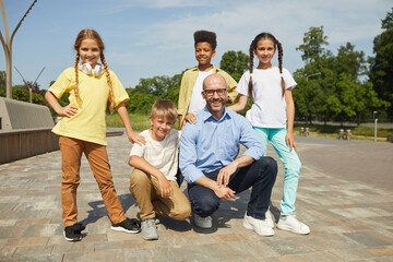 Wall Mural - group of cheerful teenage kids looking at camera while posing with smiling male teacher outdoors in 