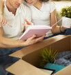 © lenets_tan - Cute couple unpacking cardboard boxes in their new home, sitting on the floor and looking at a family album