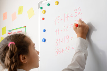 Schoolgirl calculating figures on the whiteboard, having lesson of math in school, showing her knowledge near the blackboard