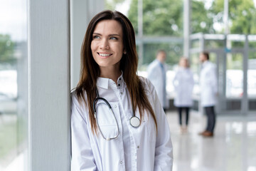 Wall Mural - Portrait of young woman doctor with white coat standing in hospital.