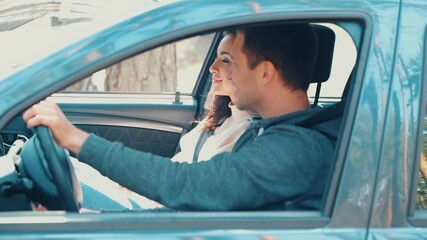 Wall Mural - Young man and woman riding together in car in forest. Happy positive cheerful couple driving together. Look at each other and smile. Small vacation time and riding in nature.