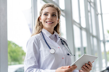 Wall Mural - healthcare, technology and medicine concept - smiling female doctor with stethoscope taking notes at tablet pc computer.