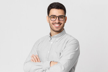 Young handsome business man wearing gray shirt and eyeglasses, holding arms crossed, smiling and feeling confident, isolated