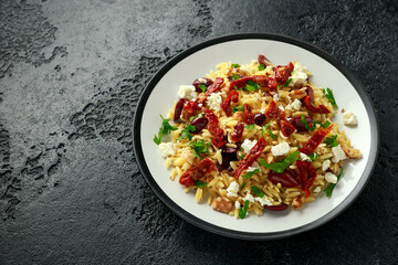 Orzo Pasta with sunshine dry tomato, black olives, walnut and feta cheese on rustic black background