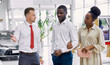 © alfa27 - beautiful black afro couple attentively listen to consultant in dealership, confident salesman talks about advantages and characteristics of car they liked