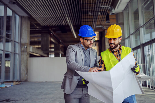 Contractor and architect looking at plan and talking about working on big project. Building in construction process interior.