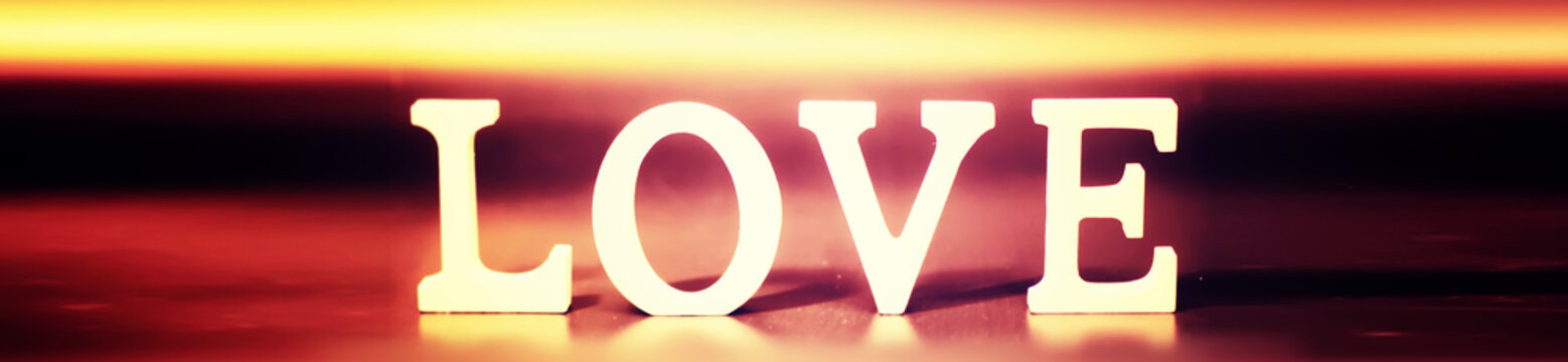 Wooden and metal letters forming word LOVE written on dark black background with lights.