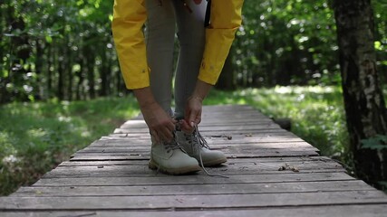 Wall Mural - hiking woman ties shoelace on hiking boots. tourist on footpath in forest