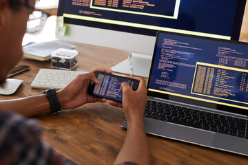 Close up of male hands holding smartphone with code on screen while working at desk in office, IT developer concept, copy space