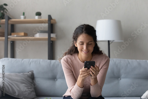 Fotografía Happy young Caucasian woman sit on couch in living room browsing internet or sho