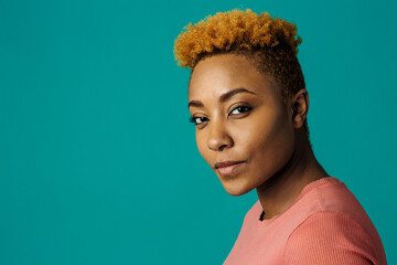 Portrait of a serious young african female with cool short hair looking at camera, against studio background