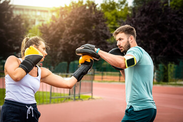 Wall Mural - Beautiful handsome healthy woman having a boxing training with personal trainer outdoors. Couple in park boxing.