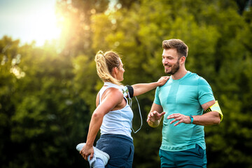 Wall Mural - Male personal trainer assisting woman with leg ecercise and talking while smiling before training in park.