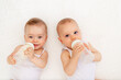 © Any Grant - two children a boy and a girl-twins of 8 months drink milk from a bottle on the bed in the nursery, feeding the baby, baby food concept, top view, place for text