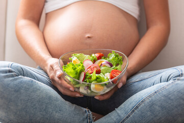 Wall Mural - Detail of a pregnant woman sitting with a fresh salad bowl in her lap