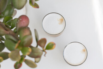 Two Glasses of coffee with cream near the leaves on white background