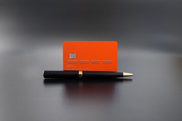 Wall Mural - Premium orange credit card with luxury pen on gray background