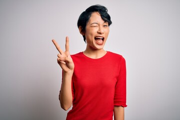 Wall Mural - Young beautiful asian girl wearing casual red t-shirt standing over isolated white background smiling with happy face winking at the camera doing victory sign with fingers. Number two.