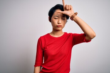 Wall Mural - Young beautiful asian girl wearing casual red t-shirt standing over isolated white background making fun of people with fingers on forehead doing loser gesture mocking and insulting.