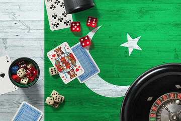 Wall Mural - Pakistan casino theme. Aces in poker game, cards and chips on red table with national wooden flag background. Gambling and betting.