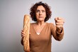 Middle age curly hair woman holding fresh homemade bread over isolated white background annoyed and frustrated shouting with anger, crazy and yelling with raised hand, anger concept