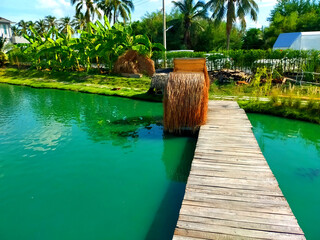 Wall Mural - Wood bridge with haystacks over a pond on green tree background