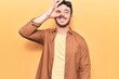 © Krakenimages.com - Young hispanic man wearing casual clothes smiling happy doing ok sign with hand on eye looking through fingers