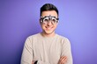 © Krakenimages.com - Young handsome caucasian man wearing optometrical glasses over purple background happy face smiling with crossed arms looking at the camera. Positive person.