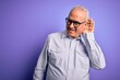 © Krakenimages.com - Middle age handsome hoary man wearing striped shirt and glasses over purple background smiling with hand over ear listening an hearing to rumor or gossip. Deafness concept.