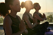 © insta_photos - Calm serene sporty young african american ethnic woman meditate sit namaste eyes closed doing breathing exercises practice relaxing at outdoor group multiethnic yoga class in morning sunrise light.