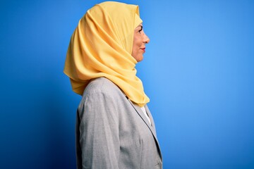 Middle age brunette business woman wearing muslim traditional hijab over blue background looking to side, relax profile pose with natural face and confident smile.