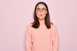 Young beautiful brunette woman wearing casual sweater and glasses over pink background making fish face with lips, crazy and comical gesture. Funny expression.