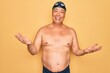 © Krakenimages.com - Middle age senior grey-haired swimmer man wearing swimsuit, cap and goggles smiling cheerful with open arms as friendly welcome, positive and confident greetings