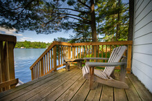 Adirondack Chair Sitting On A Cottage Wooden Deck Facing A Calm Lake During A Summer Day In Muskoka, Ontario Canada.
