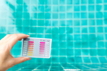 Wall Mural - Pool tester test kit in girl hand with space on blurred clear swimming pool water background, water quality for healthy and safe water for swim, summer outdoor day light 