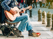 Man In A Plaid Shirt And Jeans Playing Guitar On The Street For A Living