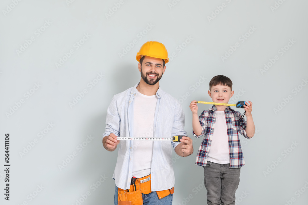Father and son with measuring tapes on grey background