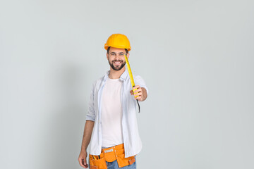 Young man with measuring tape on light background