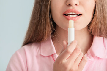 Poster - Beautiful young woman with lip balm on light background, closeup