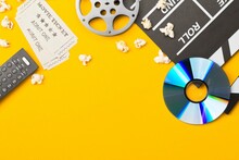 Movie Clapper Or Clapper-board With Dvd Movie Disc, Film Reel, Popcorn, Remote Control And Movie Theatre Tickets Flat Lay Top View From Above On Yellow - Home Cinema Or Movie Night Concept