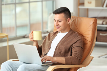 Canvas Print - Handsome young man with laptop drinking tea at home