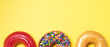Top view of chocolate frosted donut with sprinkles, sugar-glazed frosted and strawberry glazed donut on yellow background. Playful and joyful tasty sugary comfort food with copy space.