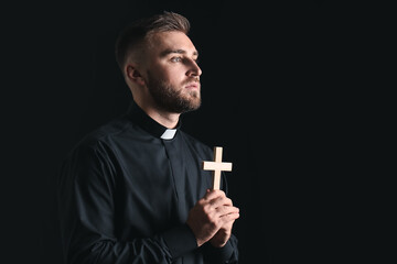Wall Mural - Young priest praying to God on dark background