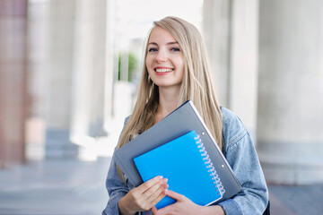 Female student outdoors holding a notebook and smiling