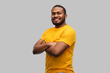 people concept - smiling young african american man in yellow t-shirt with crossed arms over grey background