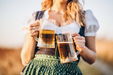 Close-up Photo Of Blonde In Dirndl, Traditional Festival Dress, Holding Two Mugs Of Beer In Her Hands