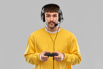 Wall Mural - technology, gaming and people concept - young man or gamer in headphones with gamepad playing and streaming video game over grey background
